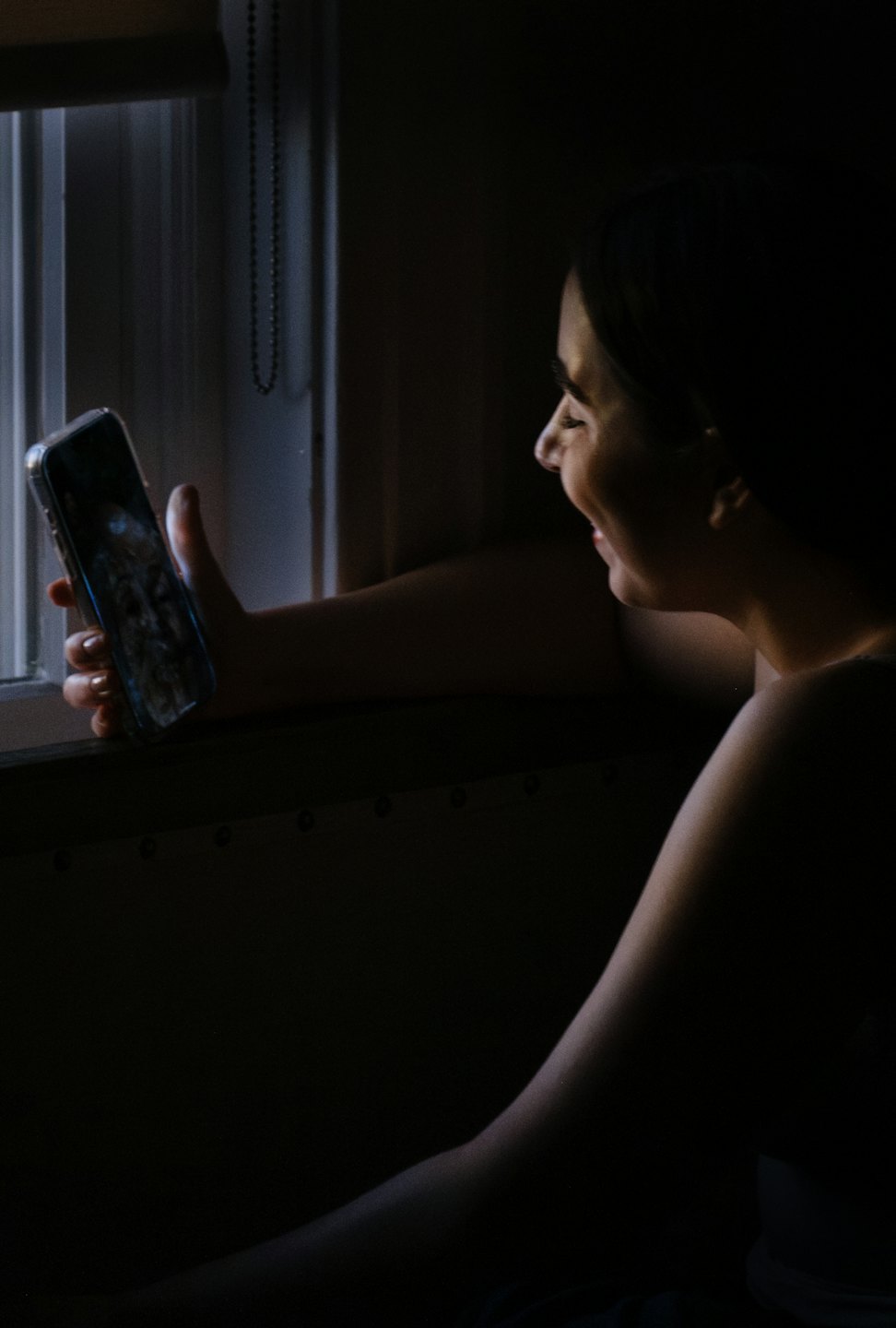 Eine Person lächelt, während sie drinnen auf ihr Smartphone schaut.