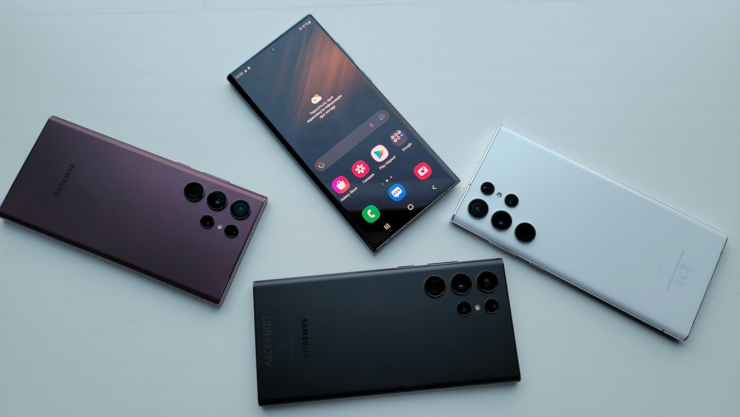 Vier Smartphones liegen auf einer weißen Oberfläche und zeigen verschiedene Farben.